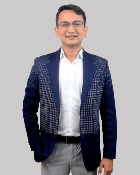 Studio portrait of Snehaashish Pathakk in a navy houndstooth blazer, white shirt and glasses, 2023.